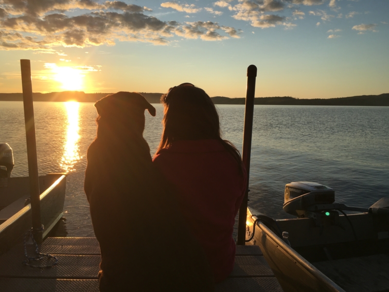 Girl and dog outline sitting on deck looking at sunset on the lake